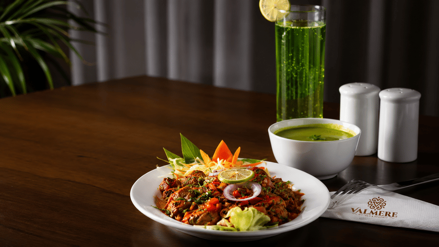 A plate of chicken starter garnished with vegetables, a side of green sauce, and a cold beverage at Valmere Lungta Boutique Hotel & Spa, Darjeeling.