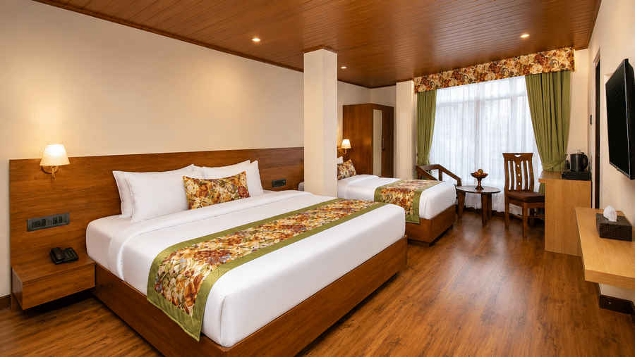 2 double beds set against a wooden headboard, lamps, wall pictures, and a door at Valmere Lungta Boutique Hotel & Spa, Darjeeling.