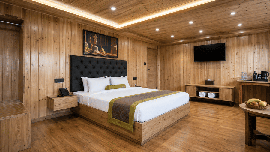 Guest room at Valmere Magnolia Boutique Hotel & Spa, Pelling with a bed, a dark headboard, a wall-mounted TV, a wooden console with towels, and a minibar tray.