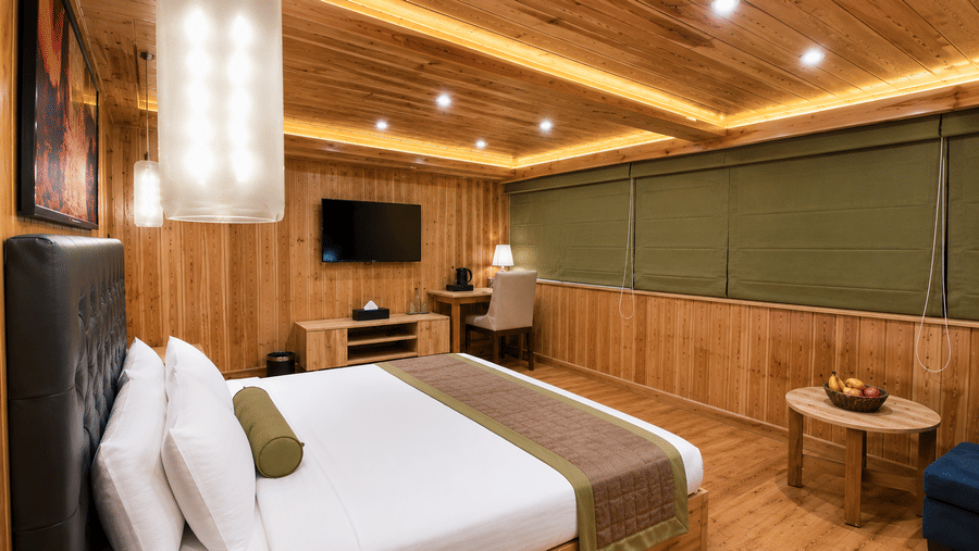 Guest room at Valmere Magnolia Boutique Hotel & Spa, Pelling with a bed, a dark headboard, a wall-mounted TV, a desk, and olive-green window blinds.