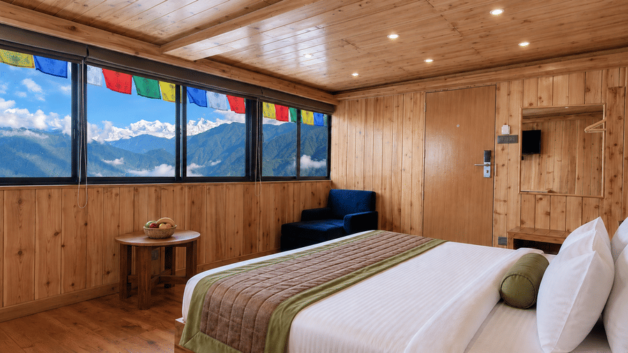Guest room at Valmere Magnolia Boutique Hotel & Spa, Pelling with a bed, a navy armchair, and a window strung with prayer flags overlooking snow-capped peaks.