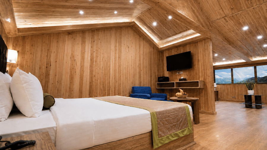 Attic Suite bedroom at Valmere Magnolia Boutique Hotel & Spa, Pelling with a sloped wood ceiling, a bed, a navy armchair, a wall-mounted TV, and mountain views.