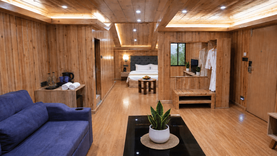 Attic Suite at Valmere Magnolia Boutique Hotel & Spa, Pelling with wood-panelled walls, a navy sofa, an open wardrobe with robes, and a view to the bedroom.