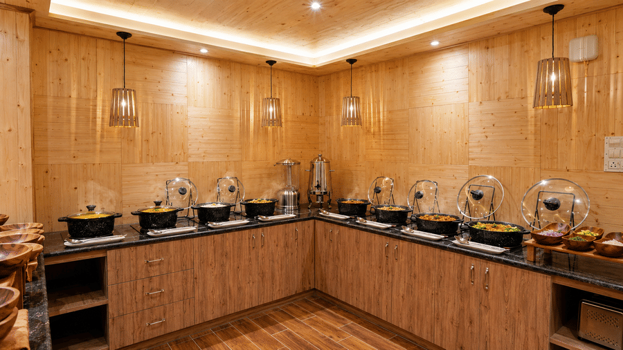Buffet counter at Valmere Magnolia Boutique Hotel & Spa, Pelling with wooden cabinetry, pendant lights, and several chafing dishes of food under glass domes.