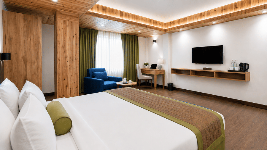 Guest room at Valmere Magnolia Boutique Hotel & Spa, Pelling with a bed, a navy sofa chair, a wooden desk, a wall-mounted TV, and a floating wood shelf.