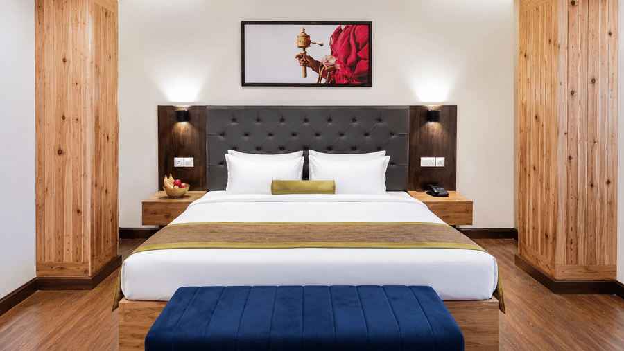 Bed at Valmere Magnolia Boutique Hotel & Spa, Pelling with a dark tufted headboard, white pillows, a fruit bowl on the nightstand, and a framed photo above.