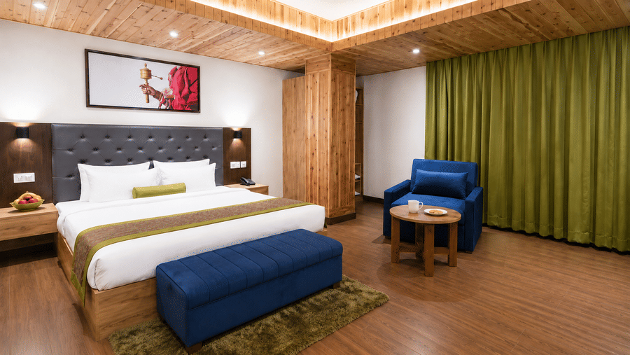 Guest room at Valmere Magnolia Boutique Hotel & Spa, Pelling with a bed, a navy armchair, a round coffee table, and floor-to-ceiling olive-green curtains.
