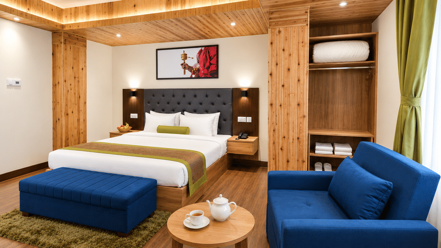 Guest room at Valmere Magnolia Boutique Hotel & Spa, Pelling with a bed, a navy sofa, a round tea table, and an open wardrobe with towels and a robe.