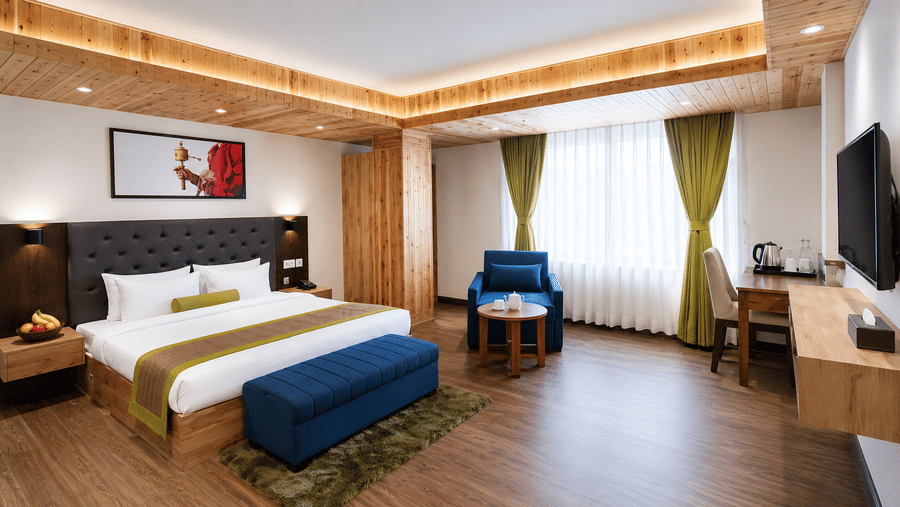 Guest room at Valmere Magnolia Boutique Hotel & Spa, Pelling with a bed, a navy armchair, a wooden desk with a chair, a wall-mounted TV, and green curtains.