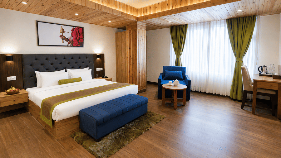 Guest room at Valmere Magnolia Boutique Hotel & Spa, Pelling with a bed, a framed prayer-wheel photo, a navy sofa and ottoman, and green curtains by the window.