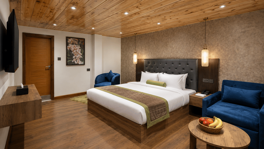 King Suite at Valmere Magnolia Boutique Hotel & Spa, Pelling with a tufted black headboard, a wall-mounted TV, a navy armchair, and a fruit bowl on a round table.