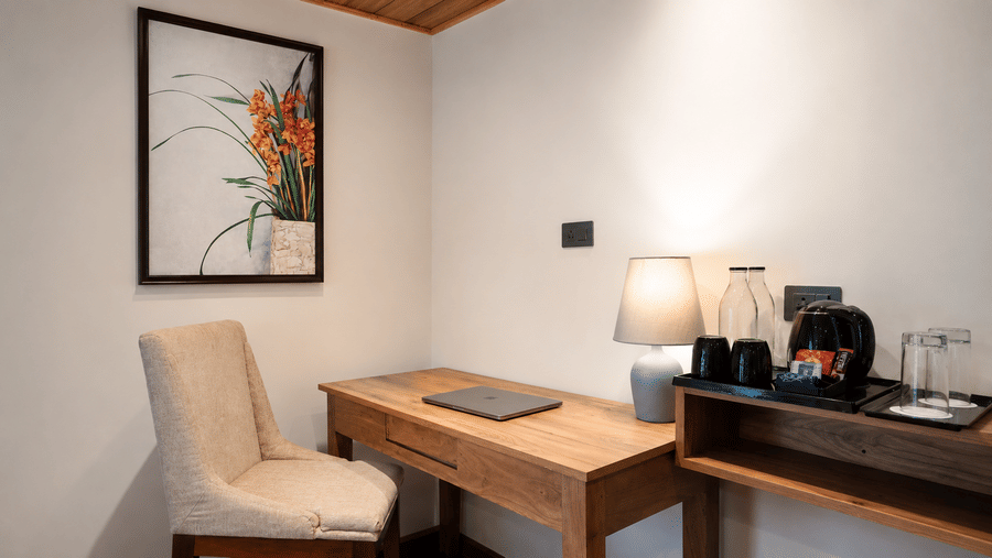 Study nook at Valmere Magnolia Boutique Hotel & Spa, Pelling with a wooden desk, beige chair, table lamp, laptop, and framed orchid artwork.