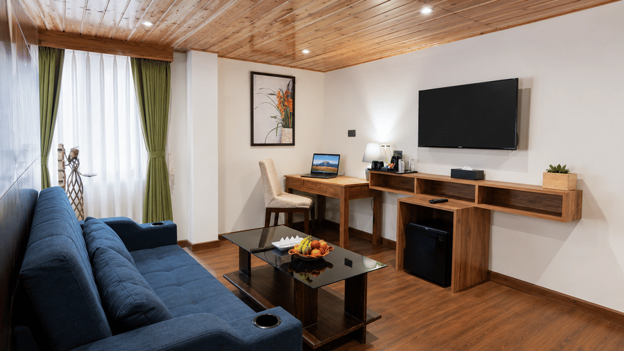 Living area at Valmere Magnolia Boutique Hotel & Spa, Pelling with a navy sofa, wall-mounted TV, wooden desk, minibar, and a glass coffee table.