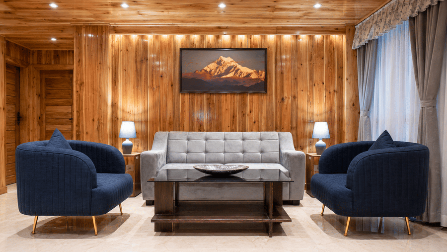 Lobby seating area at Valmere Magnolia Boutique Hotel & Spa, Pelling with a gray tufted sofa, 2 navy blue armchairs, and a framed mountain photograph.