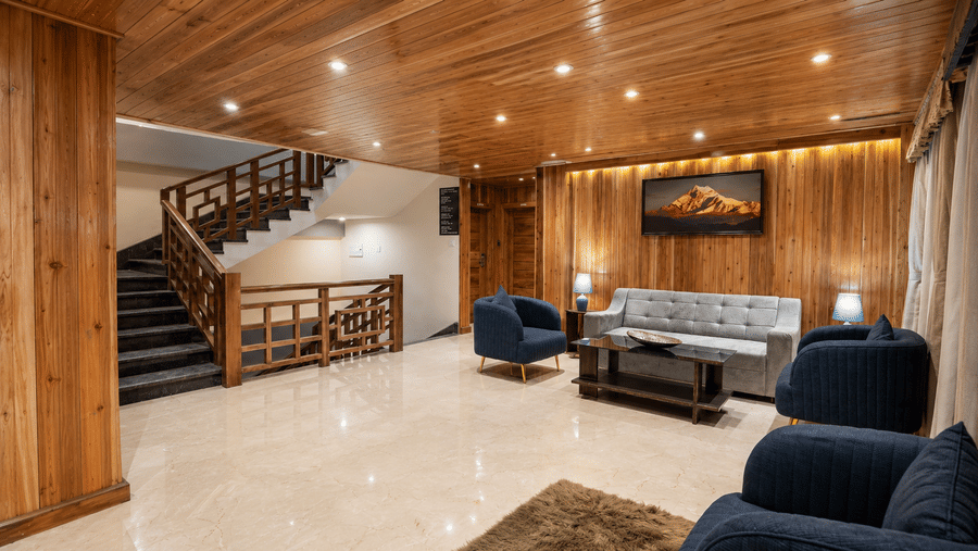 Lobby at Valmere Magnolia Boutique Hotel & Spa, Pelling with a wooden staircase, marble flooring, a grey sofa with navy blue armchairs, and mountain art.