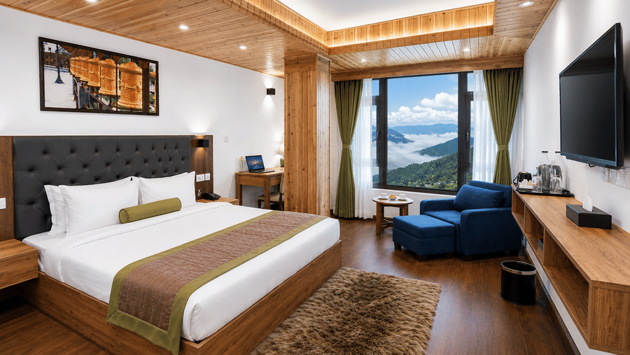 Guest room at Valmere Magnolia Boutique Hotel & Spa, Pelling with a bed, dark headboard, a navy armchair and ottoman, and a window overlooking clouds and hills.