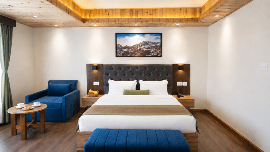 Guest room at Valmere Magnolia Boutique Hotel & Spa, Pelling with a bed, dark headboard, navy armchair, coffee table with cups, and a framed hillside photo.