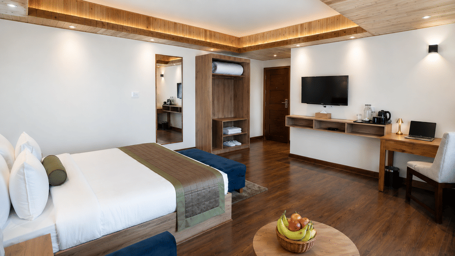 Guest room at Valmere Magnolia Boutique Hotel & Spa, Pelling with a bed, an open wardrobe with folded towels, a wall-mounted TV, and a desk.