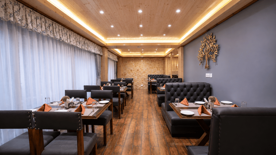 Restaurant hall at Valmere Magnolia Boutique Hotel & Spa, Pelling with black leather booths, tables set with orange napkins, and a metal tree on a blue wall.