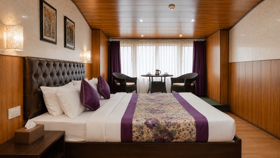 Attic Room at Valmere Thistle Boutique Hotel, Darjeeling with a king bed, purple accent pillows, and a window seating nook with wicker chairs.