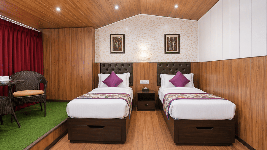 Family Room at Valmere Thistle Boutique Hotel, Darjeeling with 2 twin beds, purple accent pillows, wood-panelled walls, and a wicker seating nook.