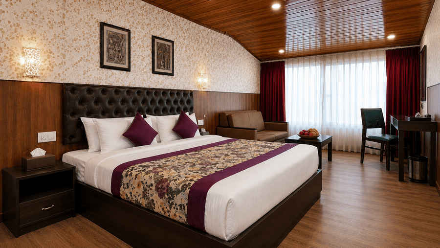 Guest room at Valmere Thistle Boutique Hotel, Darjeeling with a king bed, beige sofa, sheer curtains, and a writing desk near the window.