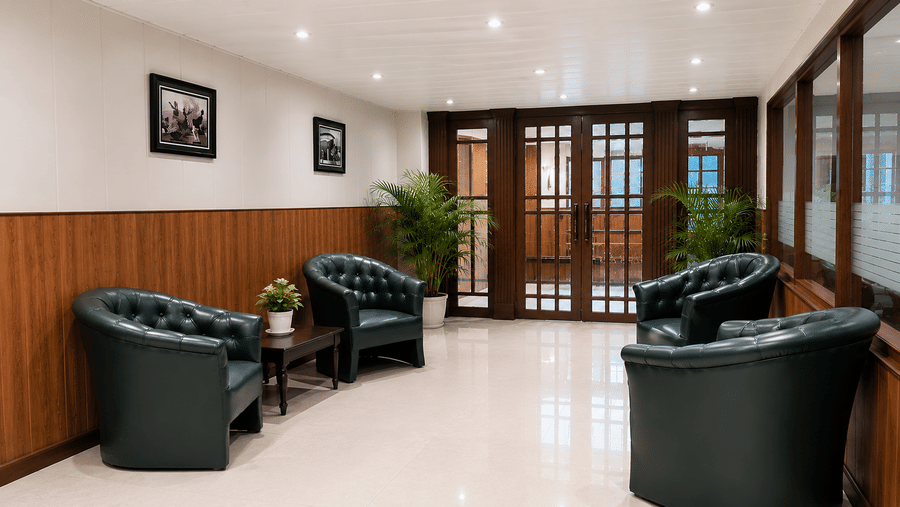 Reception seating area at Valmere Thistle Boutique Hotel, Darjeeling with dark green tufted armchairs, potted plants, and glass-paneled doors.