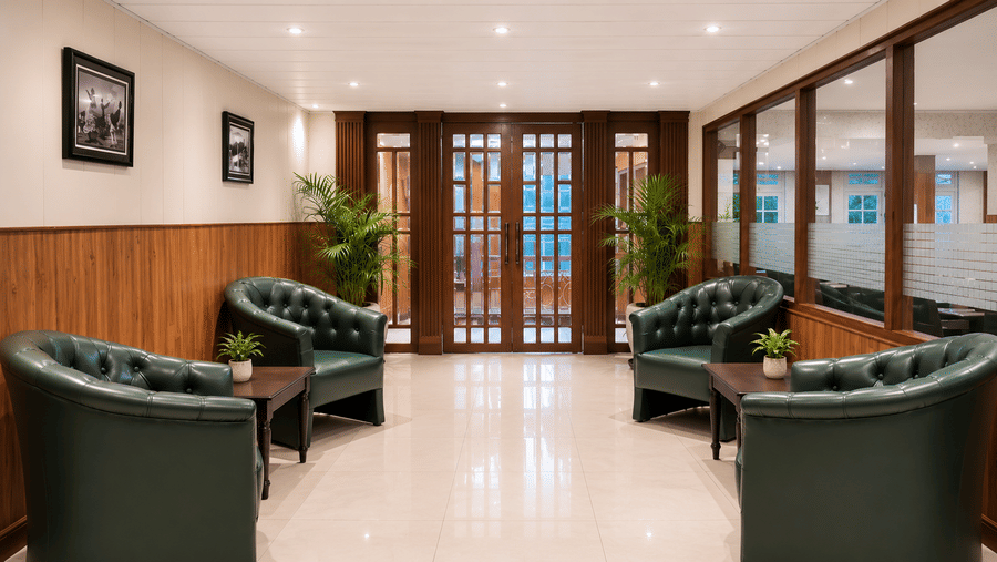 Reception seating area at Valmere Thistle Boutique Hotel, Darjeeling with dark green tufted armchairs, potted palms, and wood-framed glass doors.