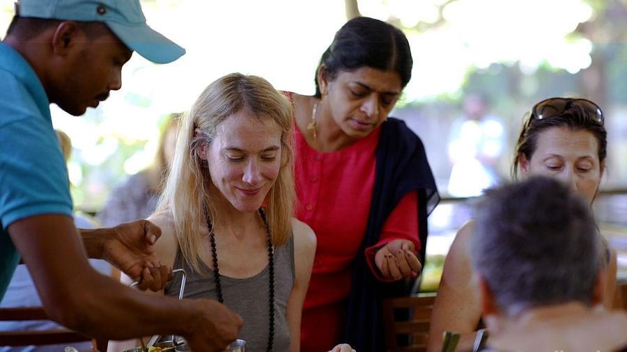A group of people are gathered around a table outdoors, sharing a meal and interacting with a server.