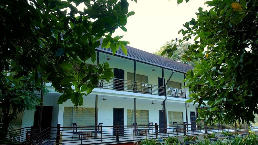 A two-story building with a porch, surrounded by a green lawn and trees.