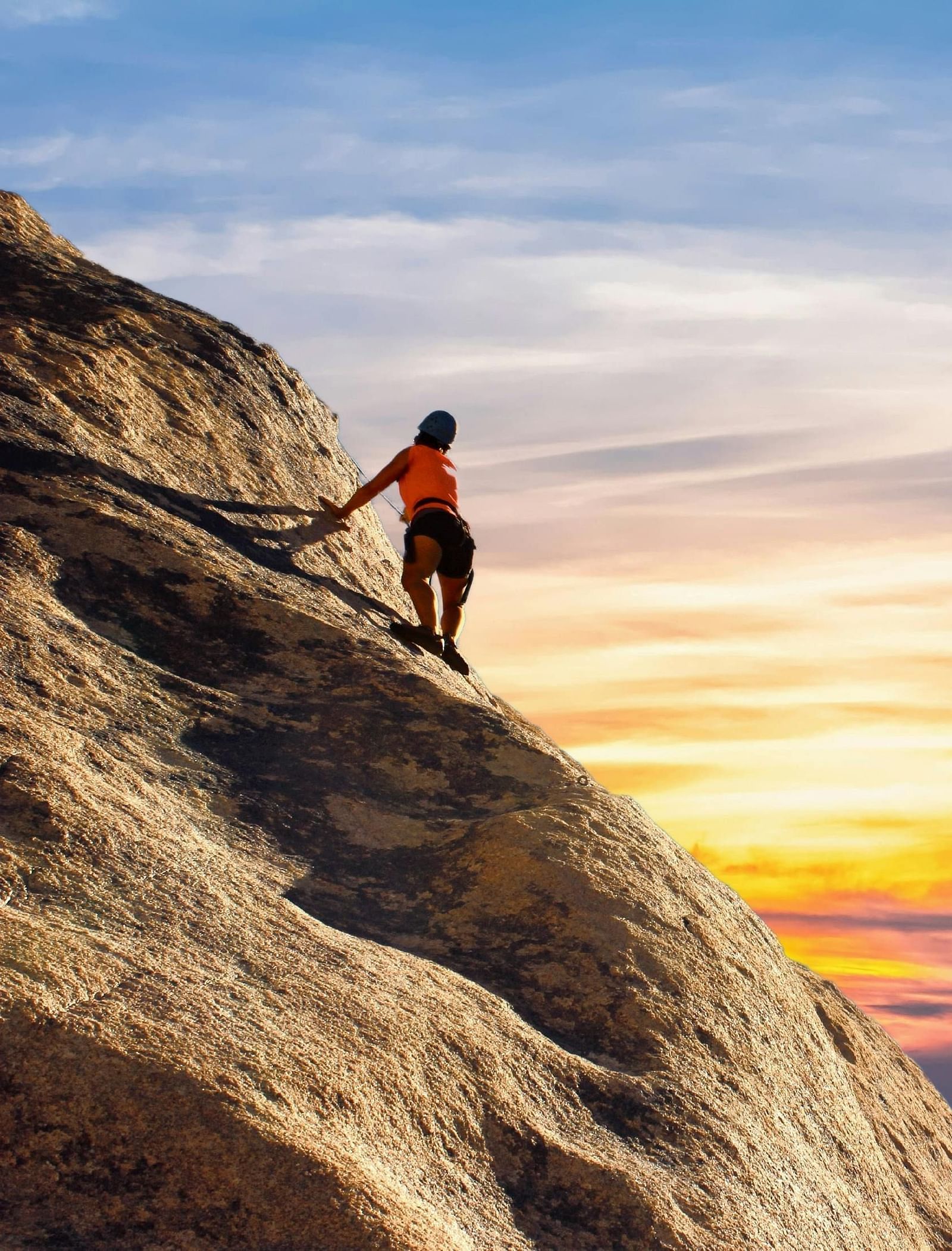 A rock climber looking at the sunset hues in the sky from the top of a mountain.