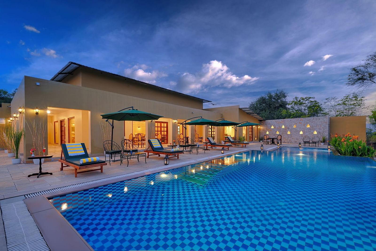 Exterior view of a resort pool with umbrellas and lounge chairs under a cloudy evening sky - Singhvilas, Ranthambore