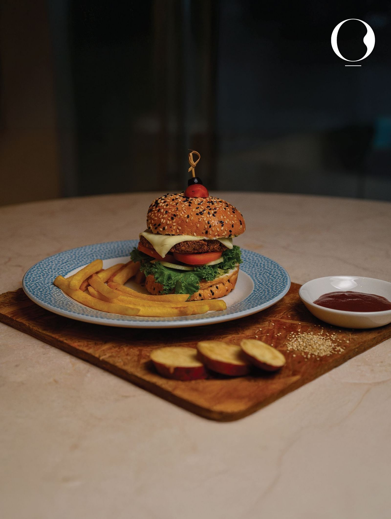 A well plated cheese burger well plated on a teal plate in a dimly lit area at Miros Hotels.
