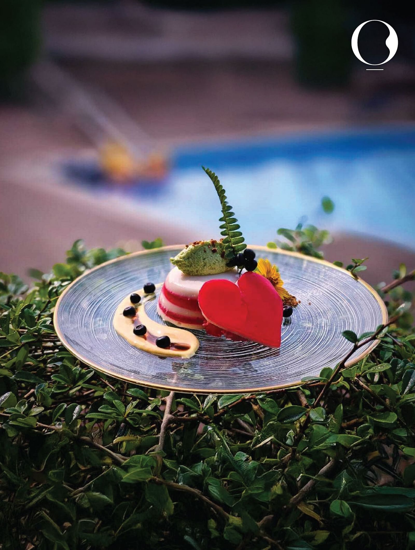 A close up of a well plated desert topped with mint leaves with the swimming pool in the background of Miros Hotels.