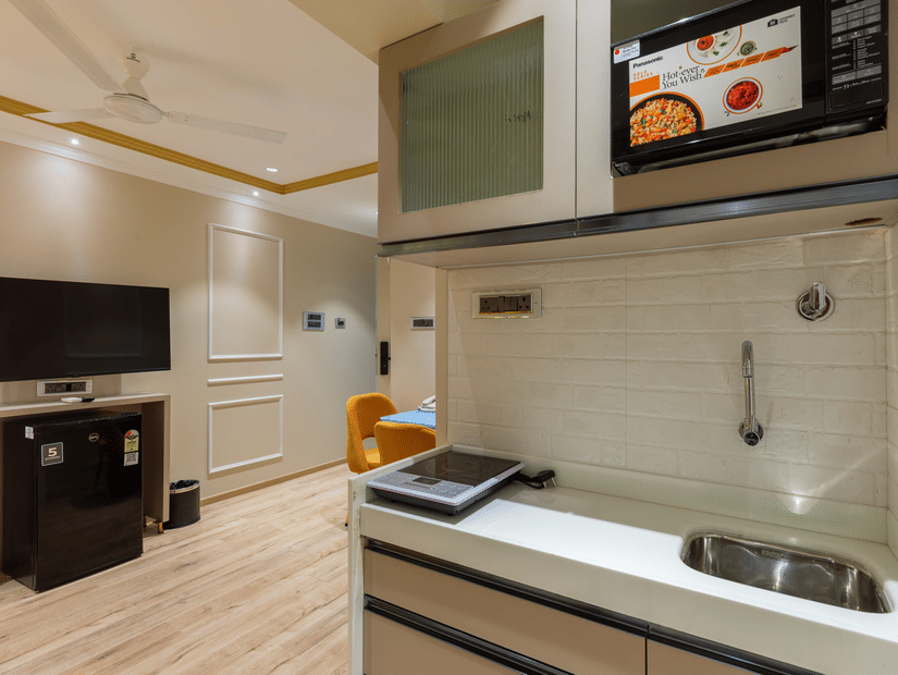 A well-equipped kitchenette at  Home2 Residency, Mumbai Airport, featuring a microwave, sink, and flat-top stove.