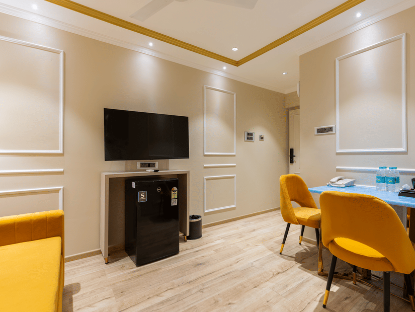 Interior view of a room at Home2 Residency, Mumbai Airport, featuring a wall-mounted TV, work desk, and vibrant yellow seating .