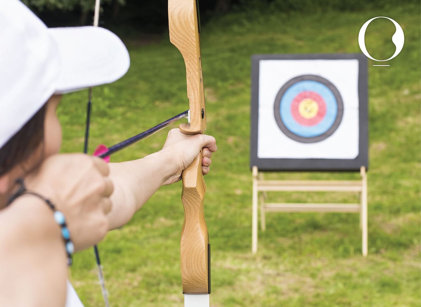 A woman aiming towards an archery board with a bow and arrow in a garden.