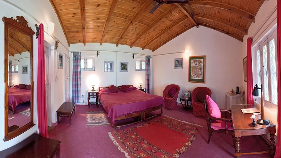 A luxury themed room with a large wall mirror, a work desk facing the window and queen size bed with wooden ceiling - Ramgarh Bungalows, Nainital.