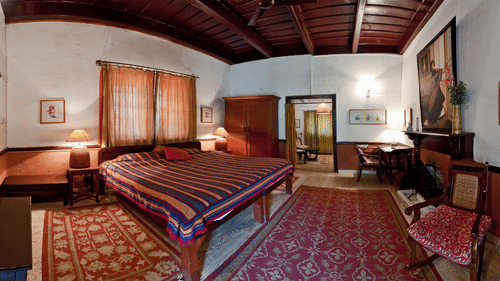 Full view of a room with cosy decor and carpeted floor along with wooden ceiling, a fireplace and a wardrobe - Ramgarh Bungalows, Nainital.