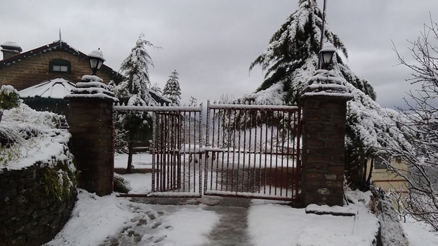 Snow covered entrance path with a closed gate and trees behind it - Ramgarh Bungalows, Nainital.