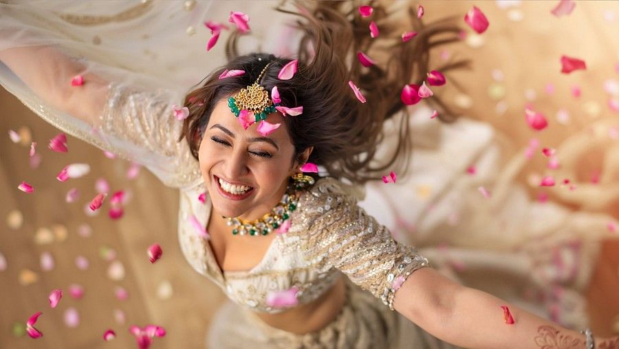 A woman in her wedding attire dancing while the flower petals are falling on her from above.