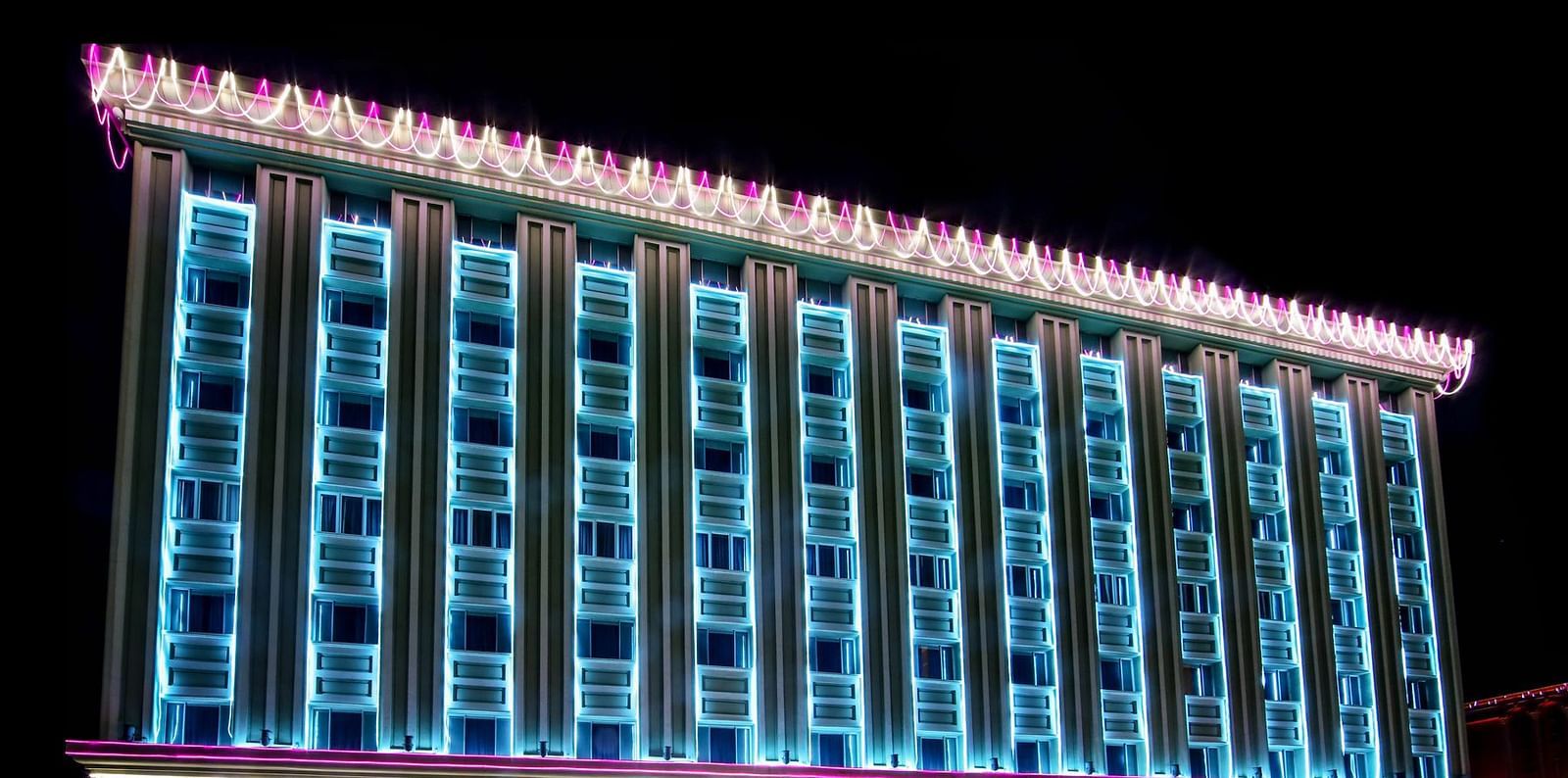 The facade of a hotel illuminated with blue neon lights at night - Tara, Comfort Hotel in Hyderabad - Ramoji Film City.