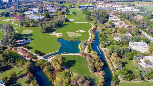 An aerial view of Karma Lakelands with waterbody, buildings and trees in view.