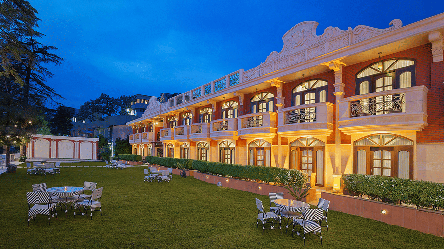 An illuminated multi-story building overlooking an outdoor lawn with seating at dusk at Ramada by Wyndham Mussoorie Mall Road.