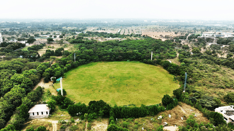 An aerial view shows a circular green sports stadium bordered by trees - District Gravity Adventure Park, Hyderabad