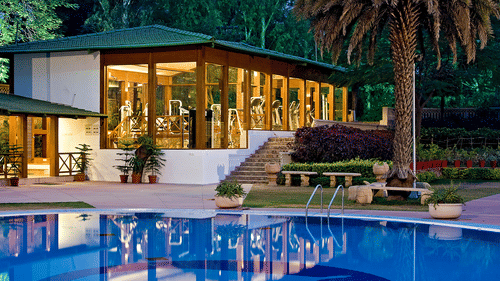 A glass-fronted fitness centre overlooking a swimming pool, surrounded by landscaped gardens and illuminated during the evening | Clarks Amer, a 5-star hotel in Jaipur near airport