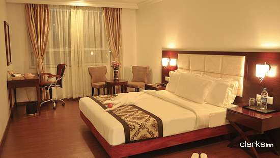 A warm-lit bedroom featuring a plush bed with nighstand and work desk as well as sitting space
