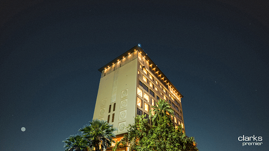 A shot of the top section of the facade of Clarks Premier, Kota in night sky lit up with warm lights and surrounded by trees