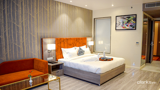A well-lit room festuring a plush bed and lamps on both sides on the nightstand and a couch with coffee table placed next to the bed