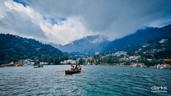 People boating on the Nainital lake amidst mountains and lush greenery under white and blue sky